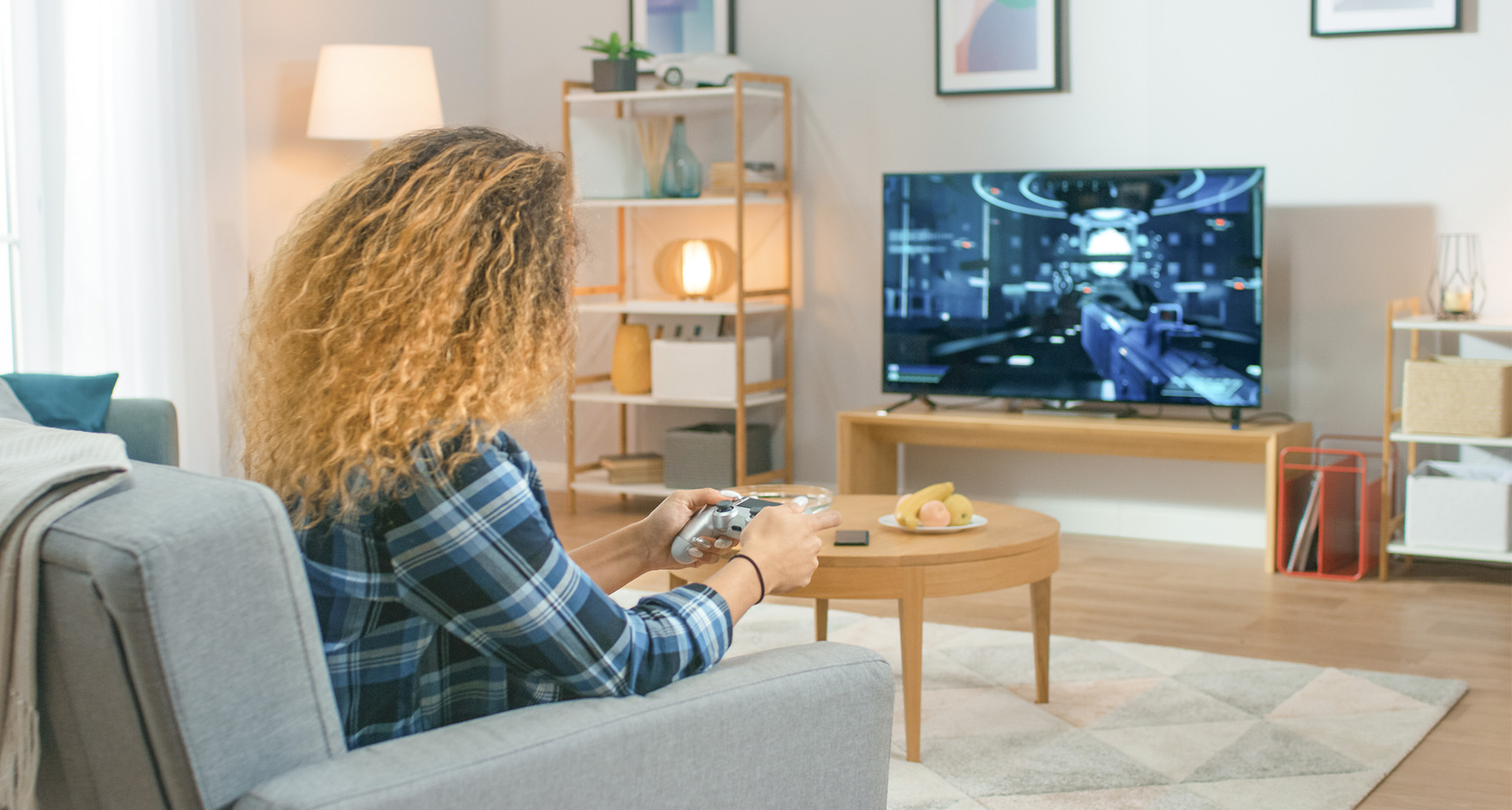 henkilö, jolla on pitkät kiharat hiukset olohuoneessa pelaamassa videopelejä televisiosta